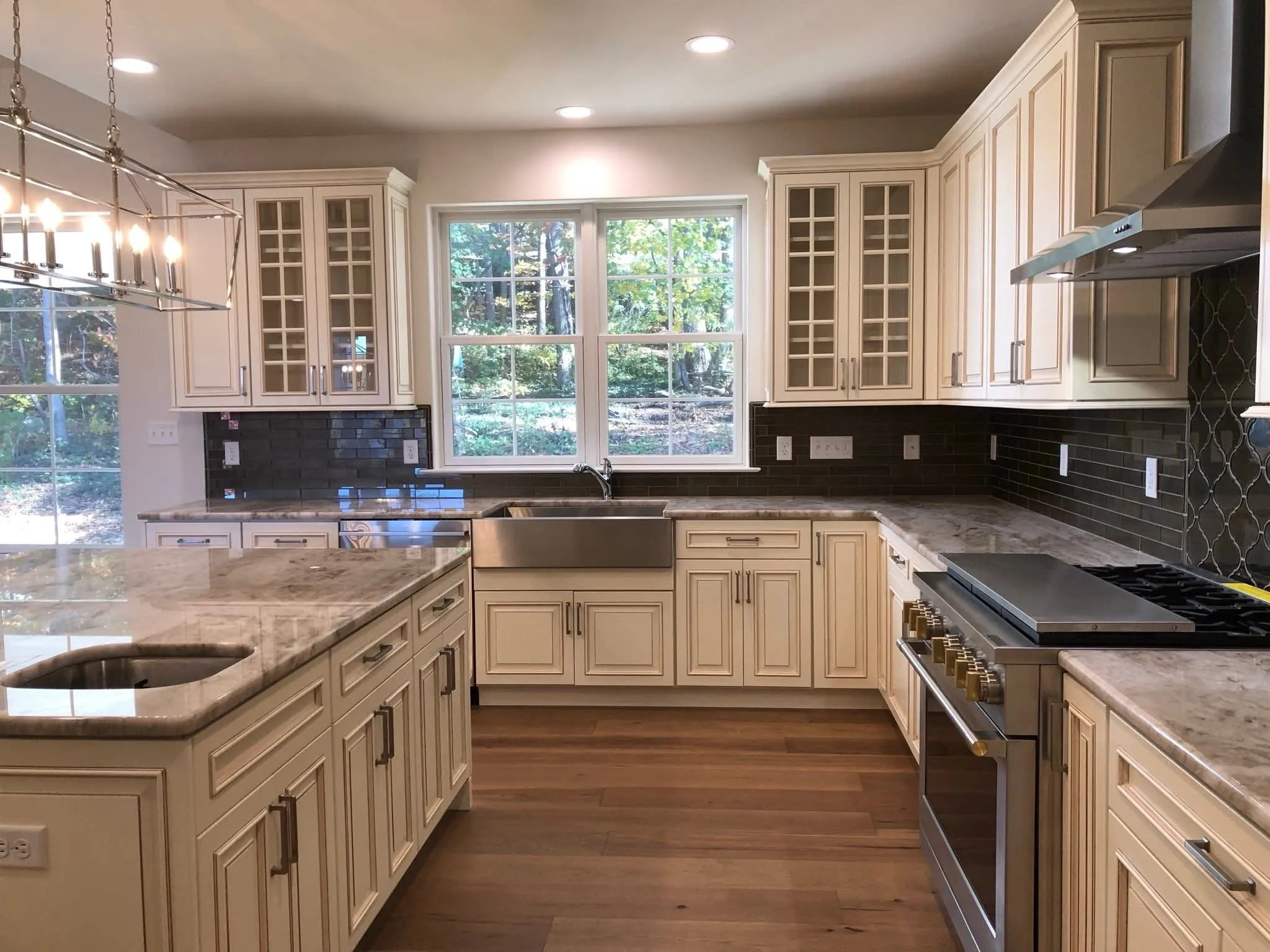 Cream colored kitchen cabinetry with glass front upper cabinets and a stainless steel farmhouse sink.